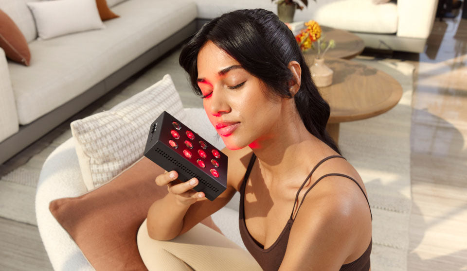 Woman holding a handheld Red Light Device towards side of face