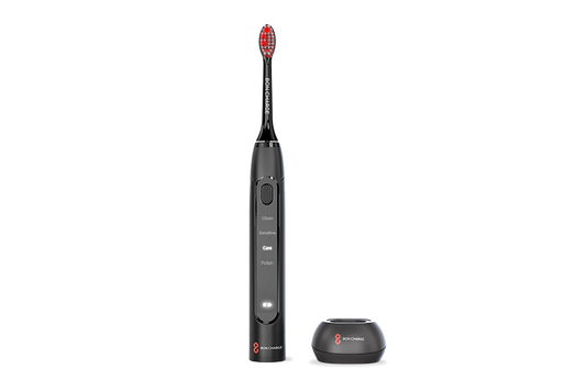 Black electric toothbrush with red bristles next to toothbrush holder